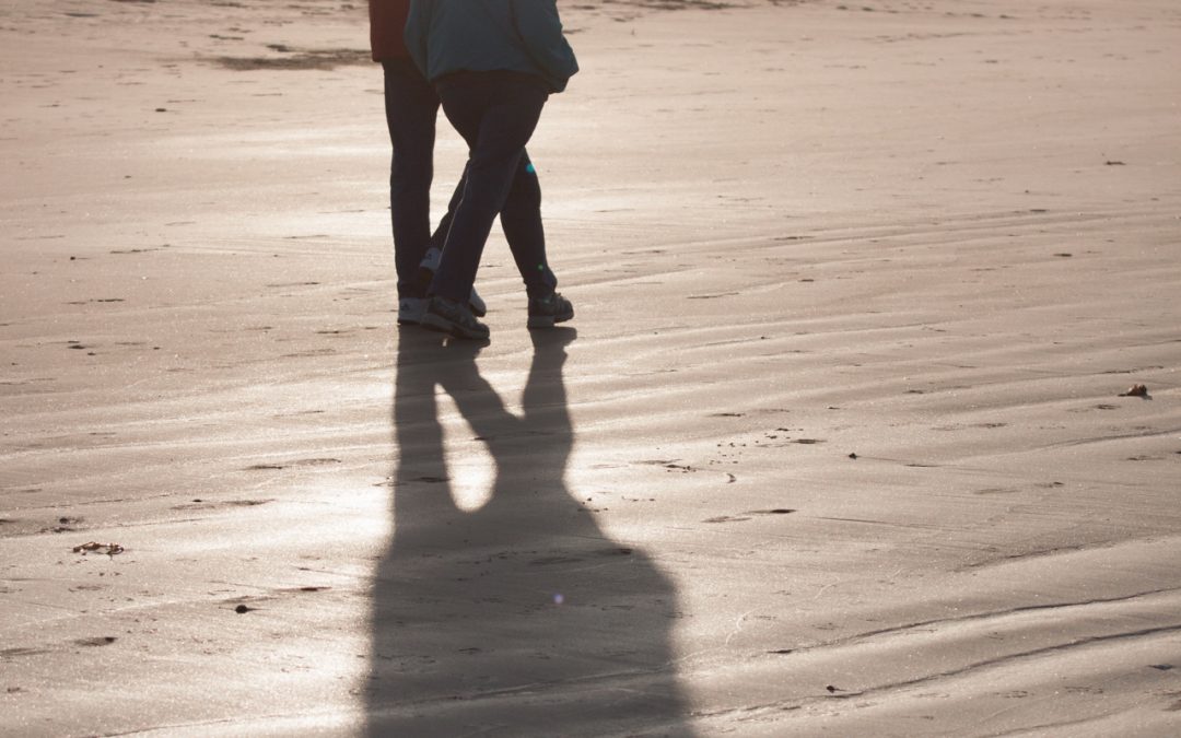 A couple walks down a beach in the early morning sun.